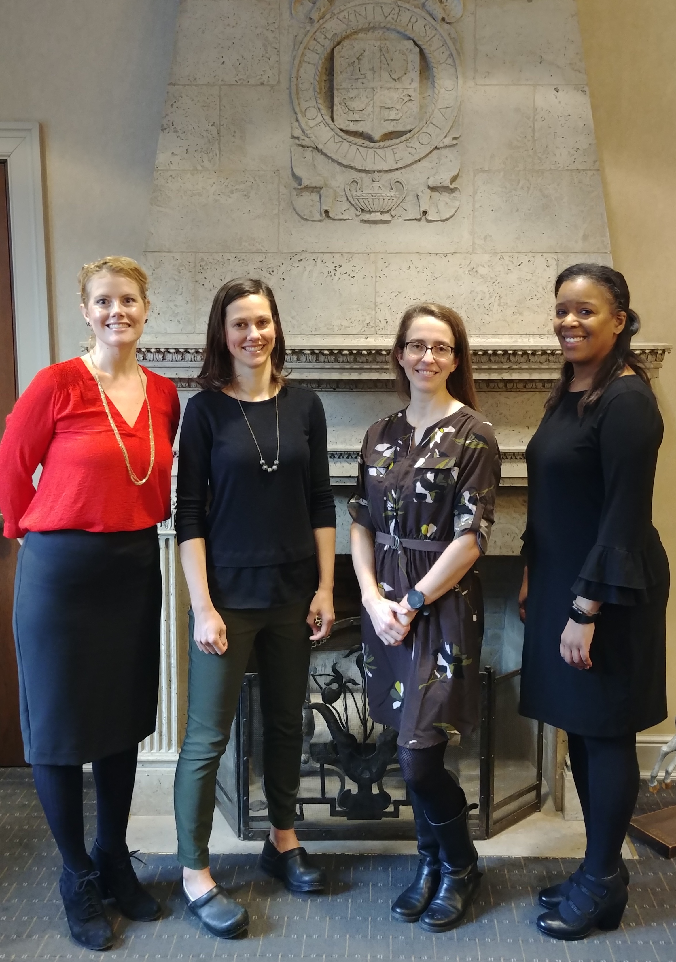 Lactation Advocacy Committee members Sara Benning, Mikaela Robertson, Sarah Keene and Equity, Access and Diversity Committee chair Keisha Varma pose in front of a fireplace topped with the U of MN seal.